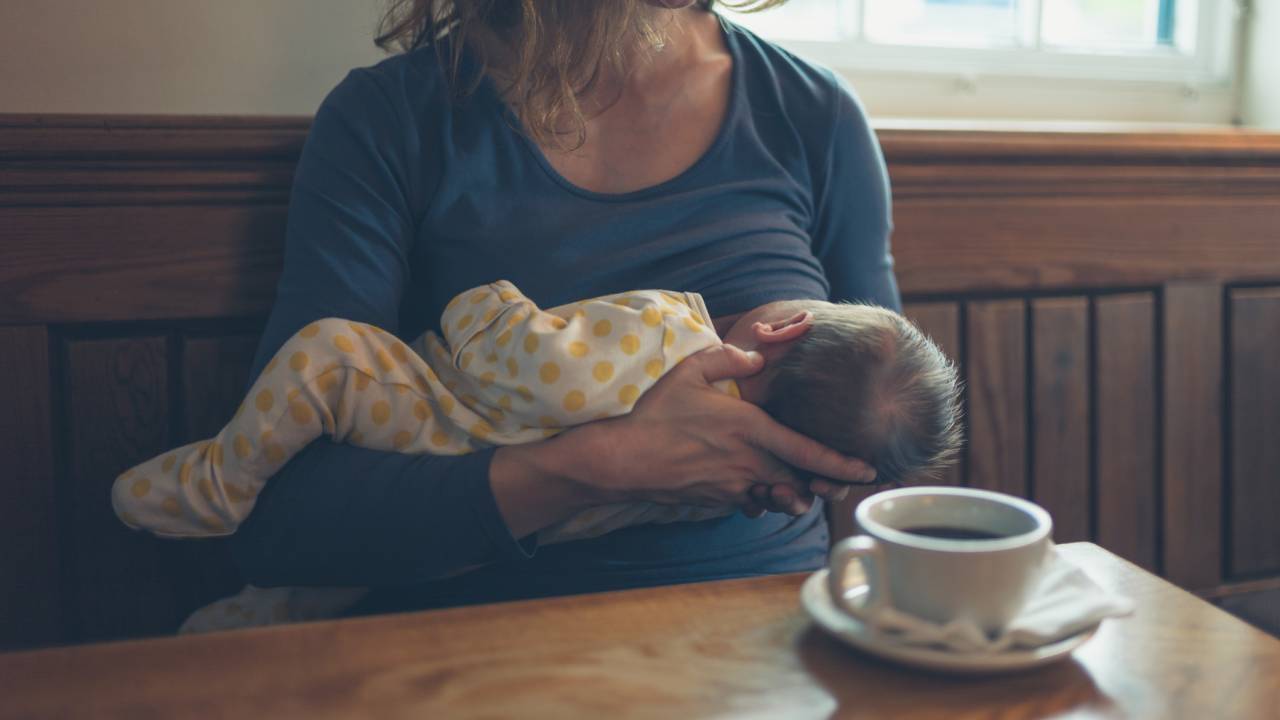 Mãe amamentando o filho em restaurante ao lado de xícara de café