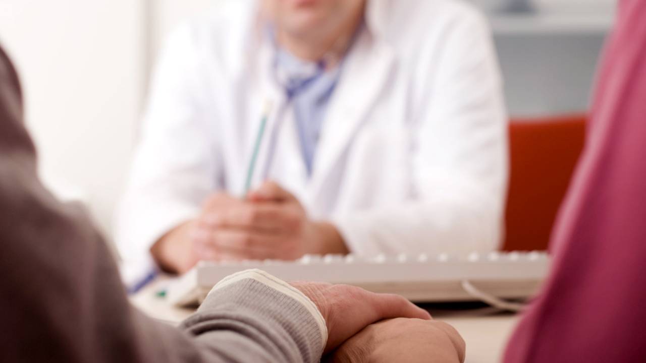Casal de mãos dadas sobre a mesa diante de médico - infertilidade