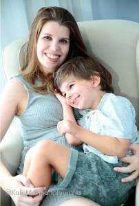 Filho de 4 anos, loiro, sentado no colo da mãe, encostado em seu peito, sorrindo, posando para uma foto junto com ela