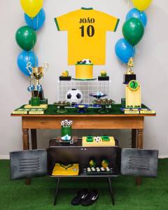 Decoração baseada em Copa do Mundo, com balões verde e amarelo, bolo em formato de bola