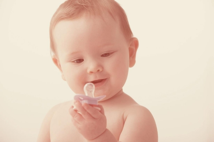 bebê olhando sorrindo para uma chupeta que está em sua mão