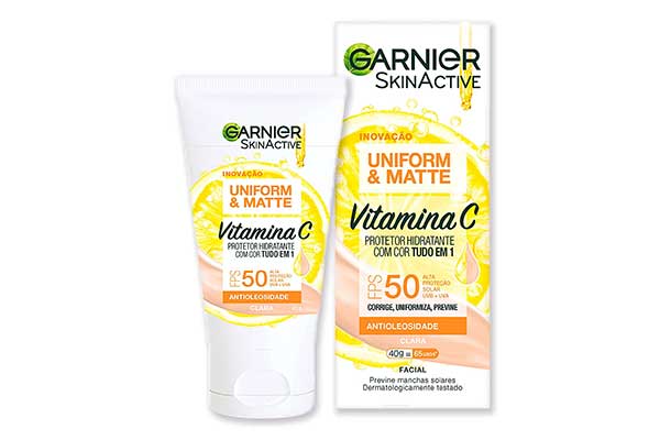 Protetor-hidratante-facial-Uniform-&-Matte-Vitamina-C-FPS-50-Garnier embalagem triangular em forma de bisnaga, posicionada com a tampa para baixo, em pé. Ao lado dela, uma caixa de papel retangular, também em pé