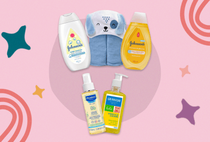 Produtos para o banho do bebê sobre fundo rosa. Há quatro embalagens de shampoos e hidratantes e uma toalha azul com roso de bichinho.