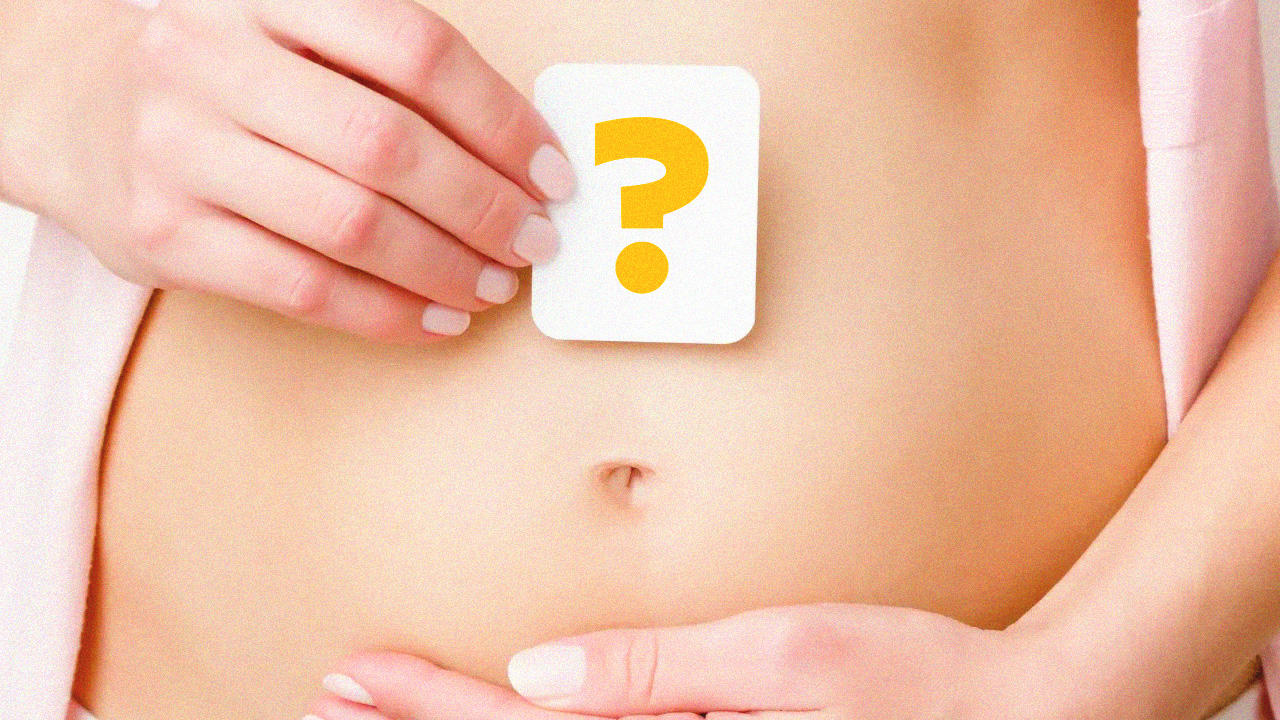 barriga de grávida ainda pequena. Está com as duas mãos sobre ela, uma delas segura um cartão com um ponto de interrogação.