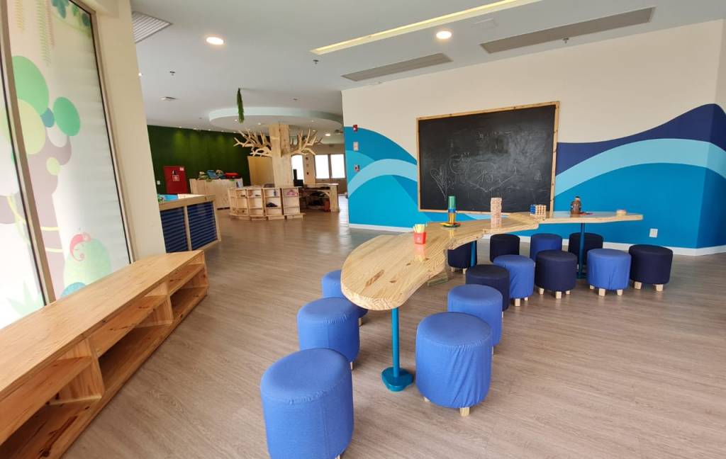 star camp iberostar recreação Na foto, uma área interna com mesa, puffs azuis e redondos, uma mesa clara e copmrida, lousa na parede, chão claro e estante de madeira.